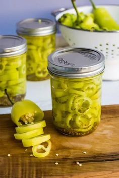 pickled green peppers in jars on a cutting board with sliced apples and spoons