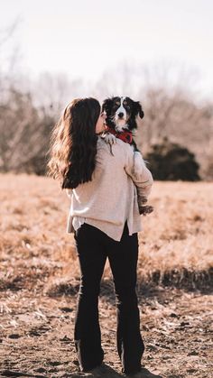 a woman holding a dog in her arms while standing on top of a dry grass field