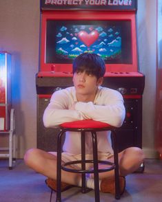 a boy sitting on the floor in front of a video game playing machine with his arms crossed