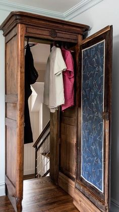 an open wooden cabinet with clothes hanging on it