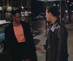 a man and woman standing on the sidewalk talking to each other in front of a car