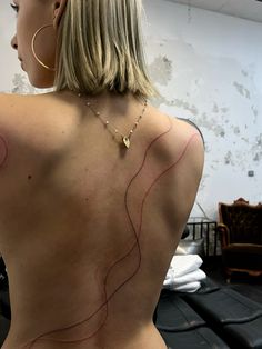 the back of a woman's body with red lines on it and a gold necklace hanging from her neck