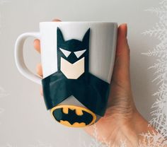 a hand holding a coffee mug with batman on it's side and snowflakes in the background