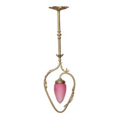 a pink glass lamp hanging from a brass chandelier with filigrees