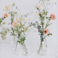 three clear vases filled with different types of flowers on a white tableclothed surface