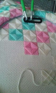 two green handled scissors sitting on top of a piece of crocheted material with pink and blue squares