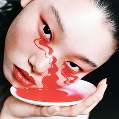 a woman with red paint on her face holding a plate in front of her face