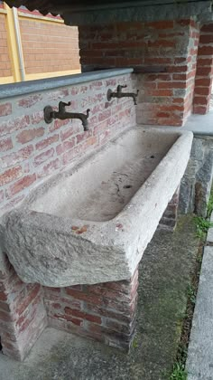 an old stone sink in front of a brick wall