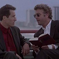 two men sitting on a bench talking to each other while one holds an open book