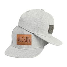 a grey hat with a leather patch on the front, and a name tag that says hudson