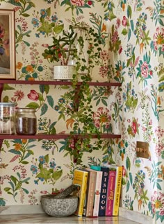 a shelf with books and vases on it in front of a wallpapered wall