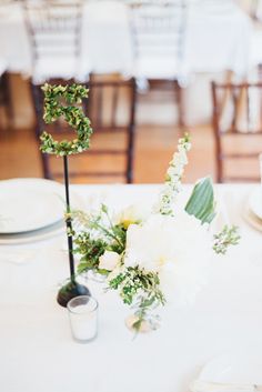 the table is set with white flowers, greenery and two black candlesticks