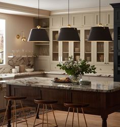 a kitchen with marble counter tops and stools in front of the center island that has three black lamps hanging from it