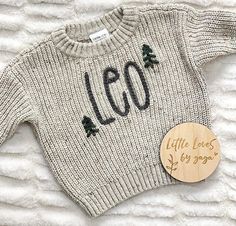 a sweater with the word leo written on it and a wooden button in front of it