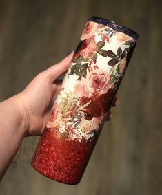 a hand holding a red and white cup with floral designs on it's side