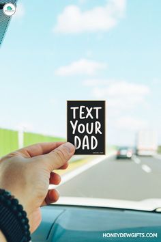 a person holding up a sign that says text your dad on the front of a car