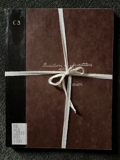 a brown and black book with a white ribbon tied around the cover on carpeted floor