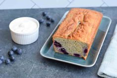 a loaf of blueberry bread on a plate next to a cup of yogurt