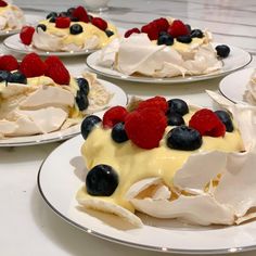 four plates with desserts on them sitting on a counter top, one has berries and the other has blueberries