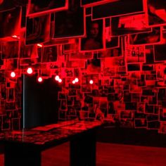 a room with red lights and pictures on the wall behind a black table in front of it