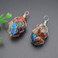 two wire wrapped pendants with multi colored stones on them sitting next to each other