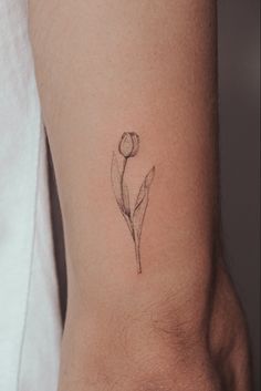 a single flower tattoo on the ankle is shown in black and grey ink, with an outline of a tulip