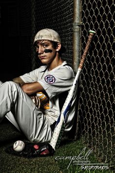 a baseball player poses with his bat in front of a chain link fence at night