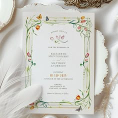 a wedding card with flowers on it next to some feathers and other items in the background