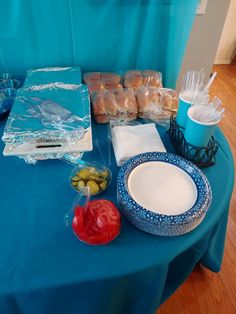 a blue table topped with plates and bowls filled with food next to plastic wrappers