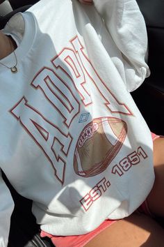 a person sitting in the back seat of a car wearing a white shirt with an orange football on it