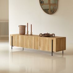 a wooden table with two vases on top and a mirror above it in a white room