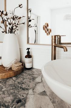 a white vase with flowers in it sitting on a bathroom counter next to a mirror