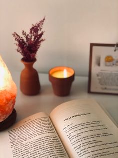 an open book sitting on top of a table next to a candle and some rocks