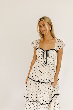 the retro-inspired dress of our dreams. it features sheer short sleeves, a ribbon tie bodice, + dainty ruffle details. both sweet + sophisticated, this off-white + black polka dot midi dress is perfect for fancy dinner dates, holiday parties, + anytime you’re feelin’ frilly. off white + black polka dots // midi length, sweetheart neckline, sheer polka dot sleeves, back zipper closure, tiered skirt, lined model is 5'8" + wearing a small measurements are approximate + taken while laying flat xsmal Cute Dresses Photoshoot, White Dress With Polka Dots, Polka Dot Bridesmaid Dresses, Polka Dot Bridesmaid Dress, Polka Dot Dress Black And White, Fun Midi Dress, Engagement Dress Casual, White Dress Black Bow, Outfit Ideas With Dresses