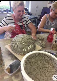 two women sitting at a table working on clay sculptures in the shape of flowers and swirls