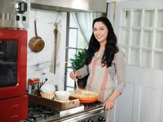 a woman standing in front of an oven holding a bowl with food on the counter