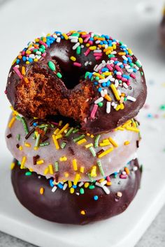 three donuts with chocolate frosting and sprinkles on a white plate