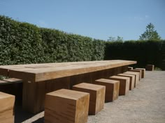 a wooden bench sitting on top of a gravel field next to a lush green hedge