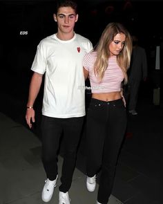 a man and woman are walking down the street at night, both wearing white sneakers