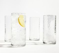 three glasses filled with water and lemon wedged in each glass, on a white background