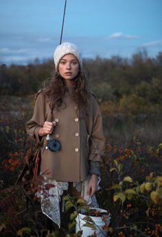 a woman standing in the middle of a field wearing a hat and holding an umbrella