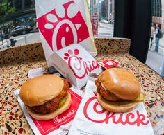 two hamburgers sitting on top of a table next to a paper bag with the word chick written on it