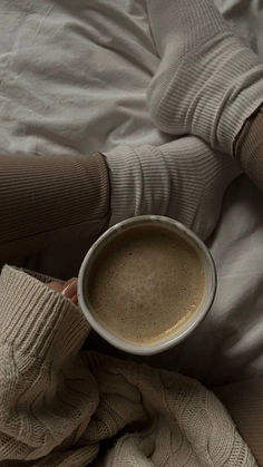 a person laying in bed holding a cup of coffee