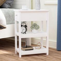 a small white shelf with an alarm clock on it next to a bed in a bedroom