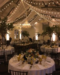 a banquet hall with tables and chairs covered in white tablecloths, decorated with lights