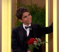 a young boy in a tuxedo holding a bouquet of flowers and smiling at the camera