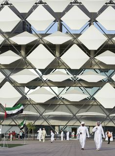 two men walking in front of a building with white walls and geometric designs on it