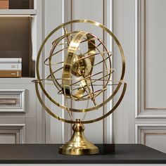 a golden metal globe on top of a black table in front of a bookcase