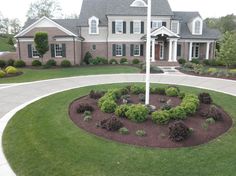 a flag pole in front of a large house with landscaping around it and bushes on the lawn