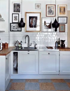 a kitchen with white cabinets and pictures on the wall above the sink, along with other items